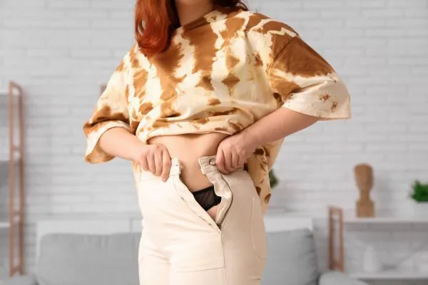 Image of woman trying to do her trousers up after pregnancy weight gain Paisley